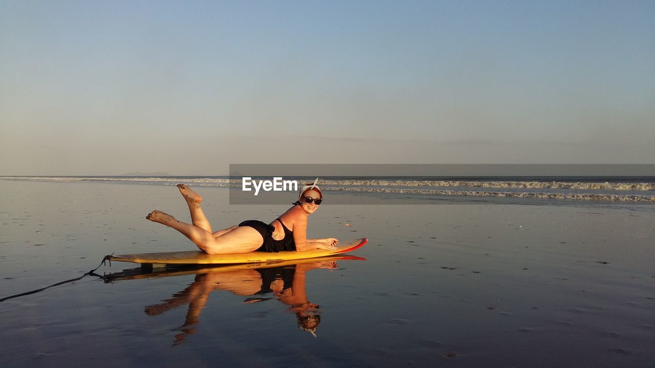 Portrait of smiling young woman in bikini lying on surfboard at beach