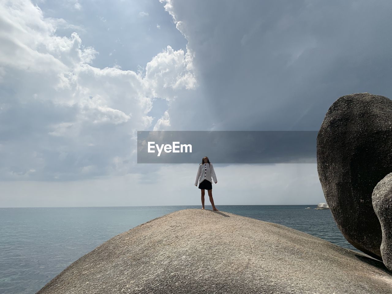 Rear view of man standing on rock by sea against sky