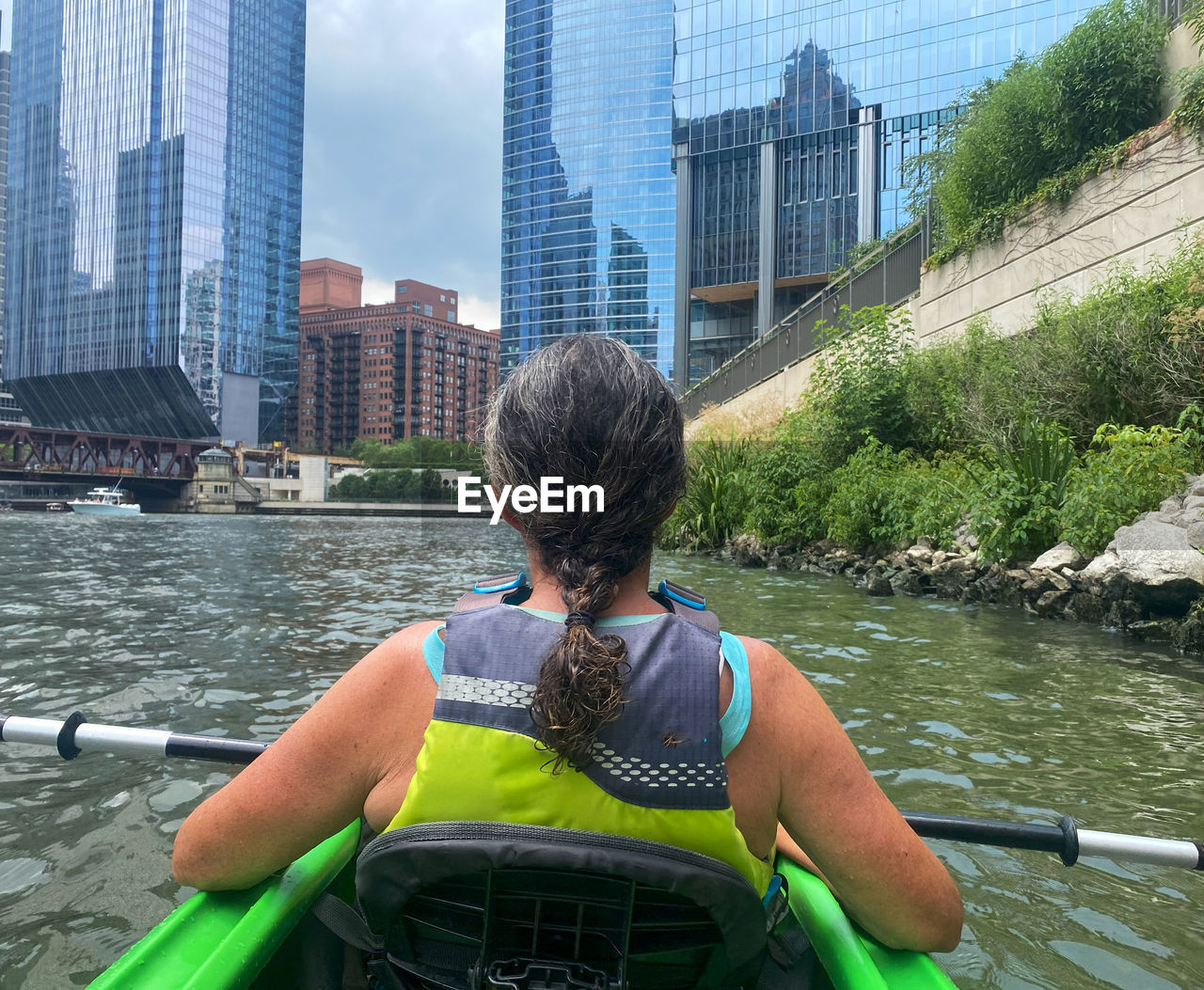 architecture, water, built structure, boating, city, building exterior, rear view, boat, one person, transportation, office building exterior, nature, vehicle, skyscraper, adult, river, day, leisure activity, building, watercraft, lifestyles, sitting, outdoors, nautical vessel, travel, city life, canoe, kayak, paddle, landscape, urban skyline, mode of transportation, sky, women, men, cityscape, travel destinations, rowing