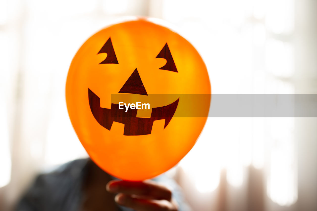 Close-up of woman holding halloween decoration against face at home