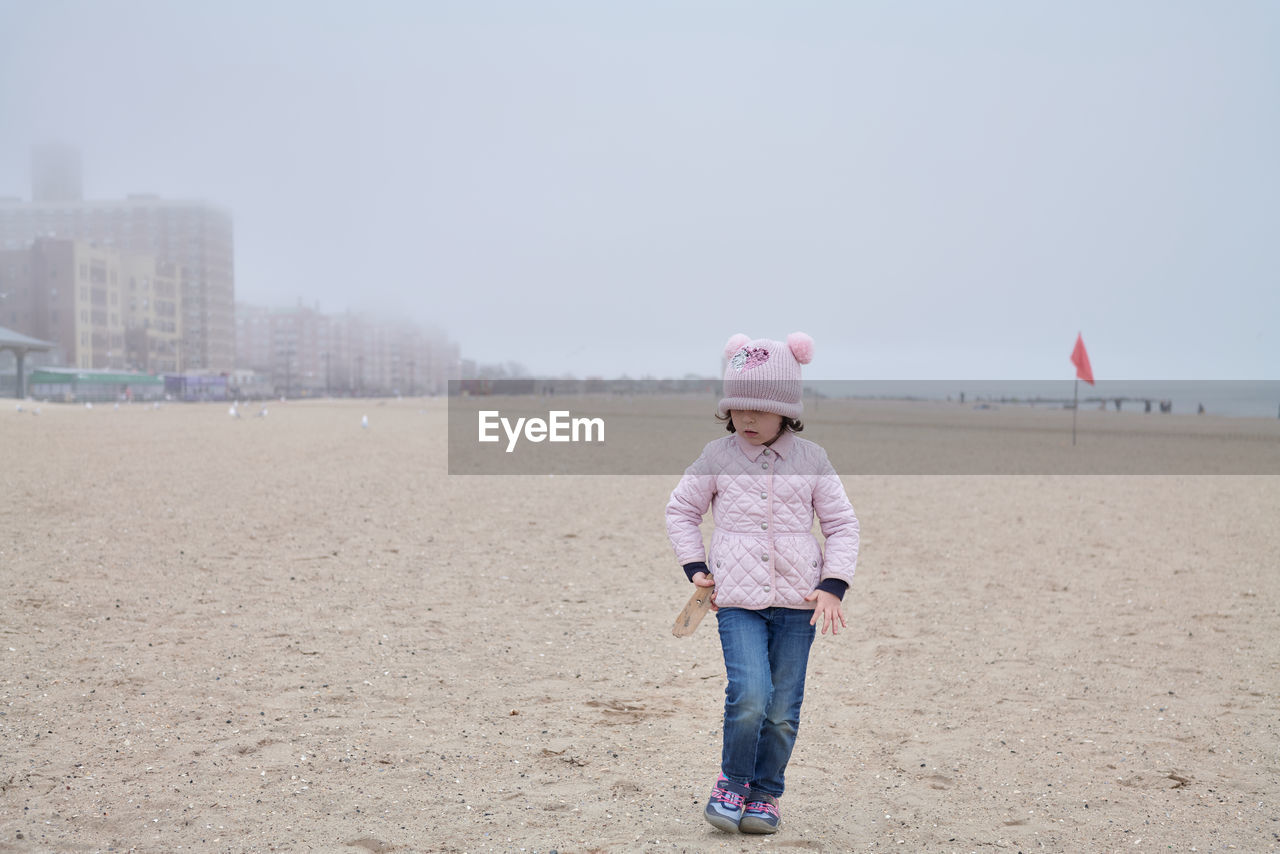 Young girl is playing on an empty beach during a foggy, cold day