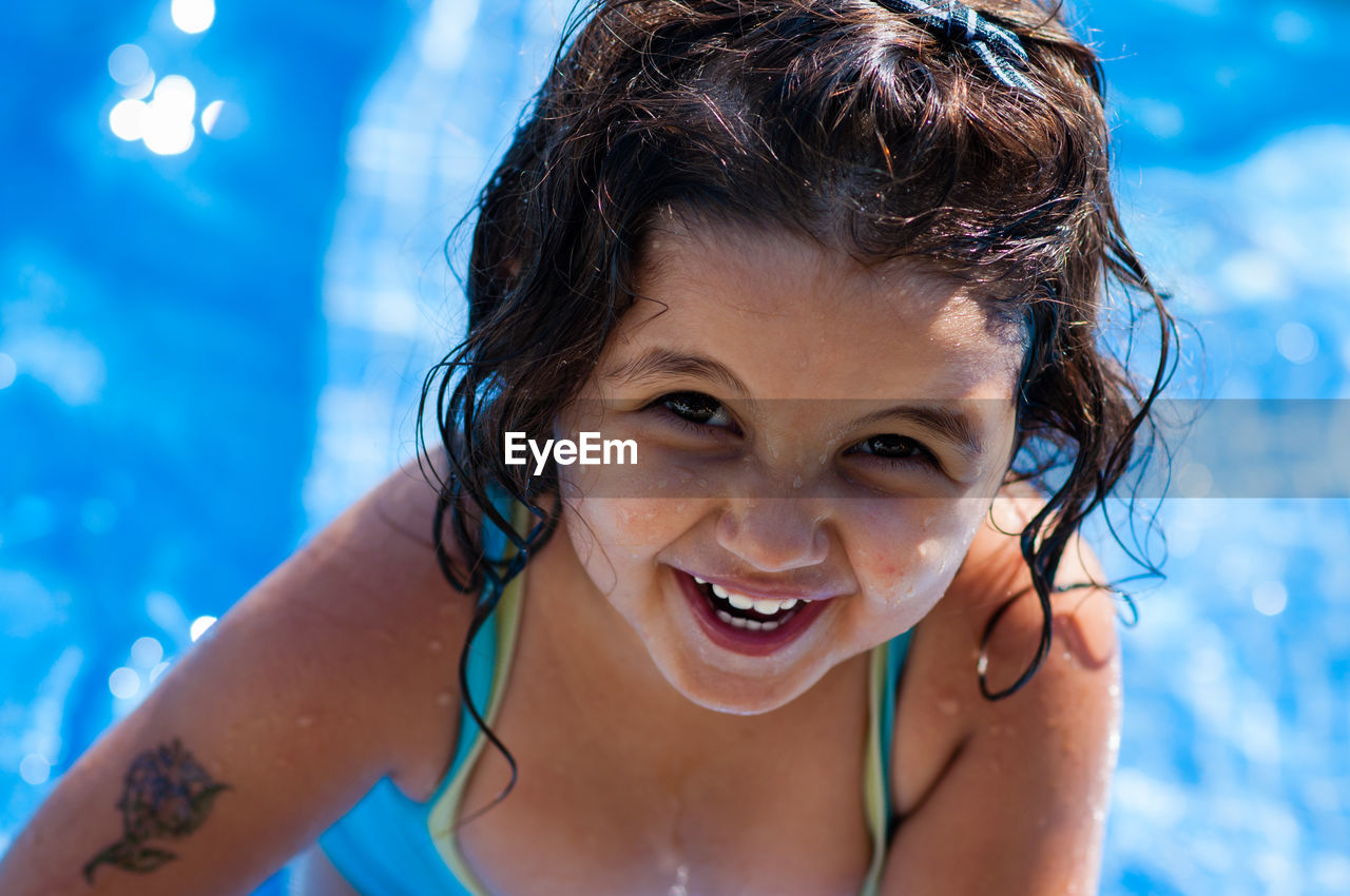 CLOSE-UP PORTRAIT OF HAPPY BOY SWIMMING IN POOL