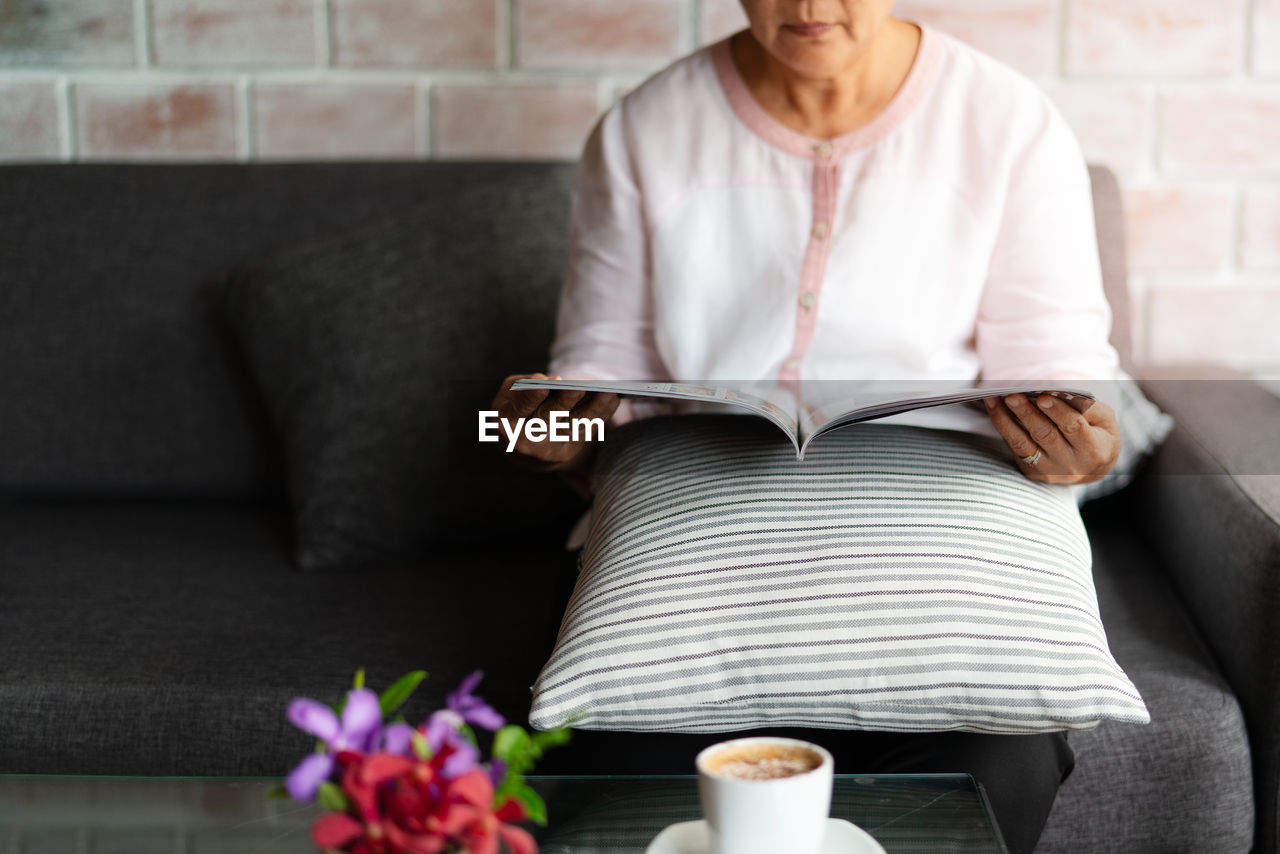 Old woman reading a book with cup of coffee at home