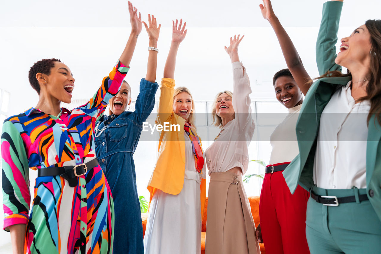 portrait of smiling friends with arms raised standing against white background