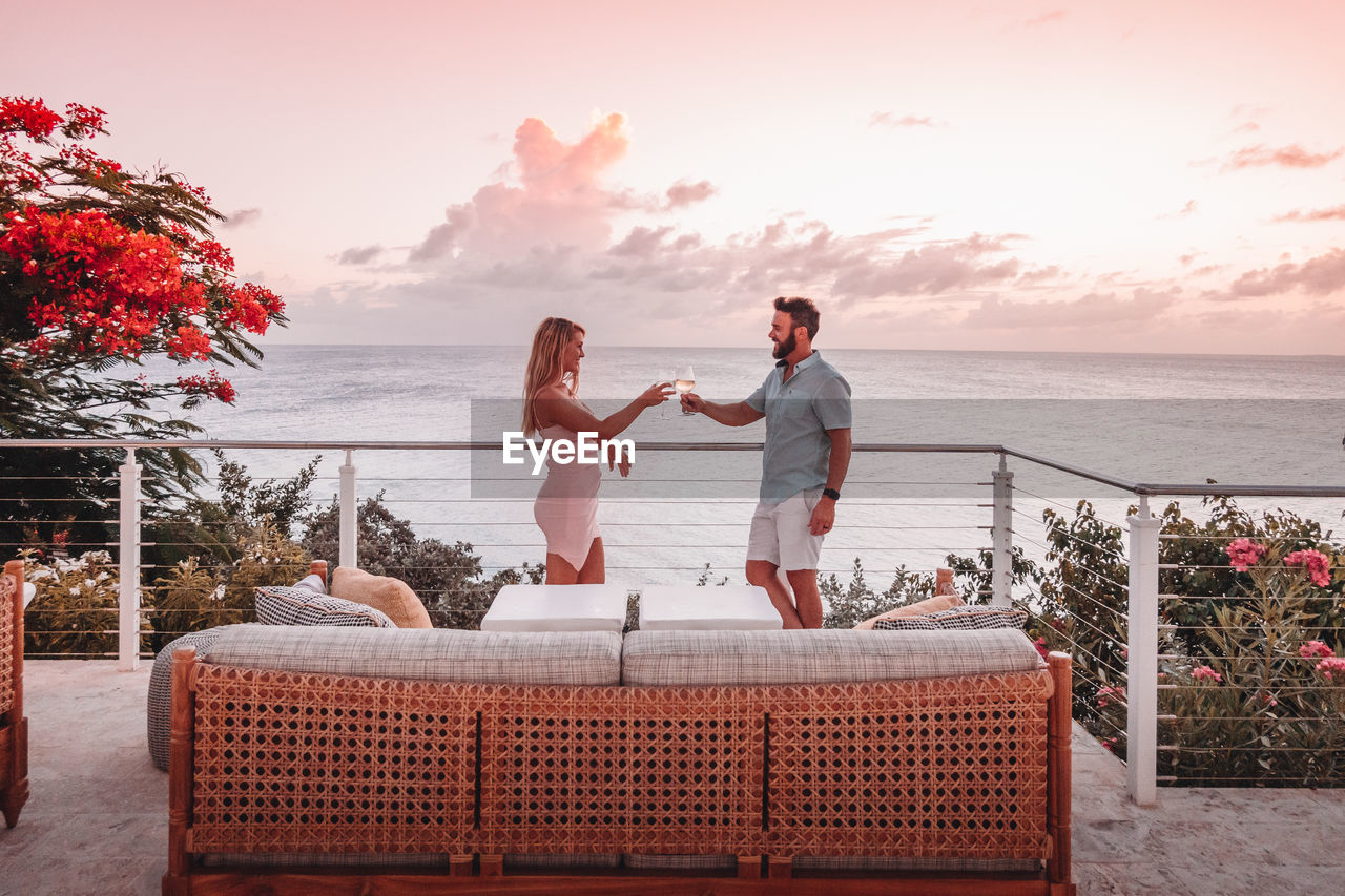 FRIENDS STANDING ON RAILING AGAINST SEA