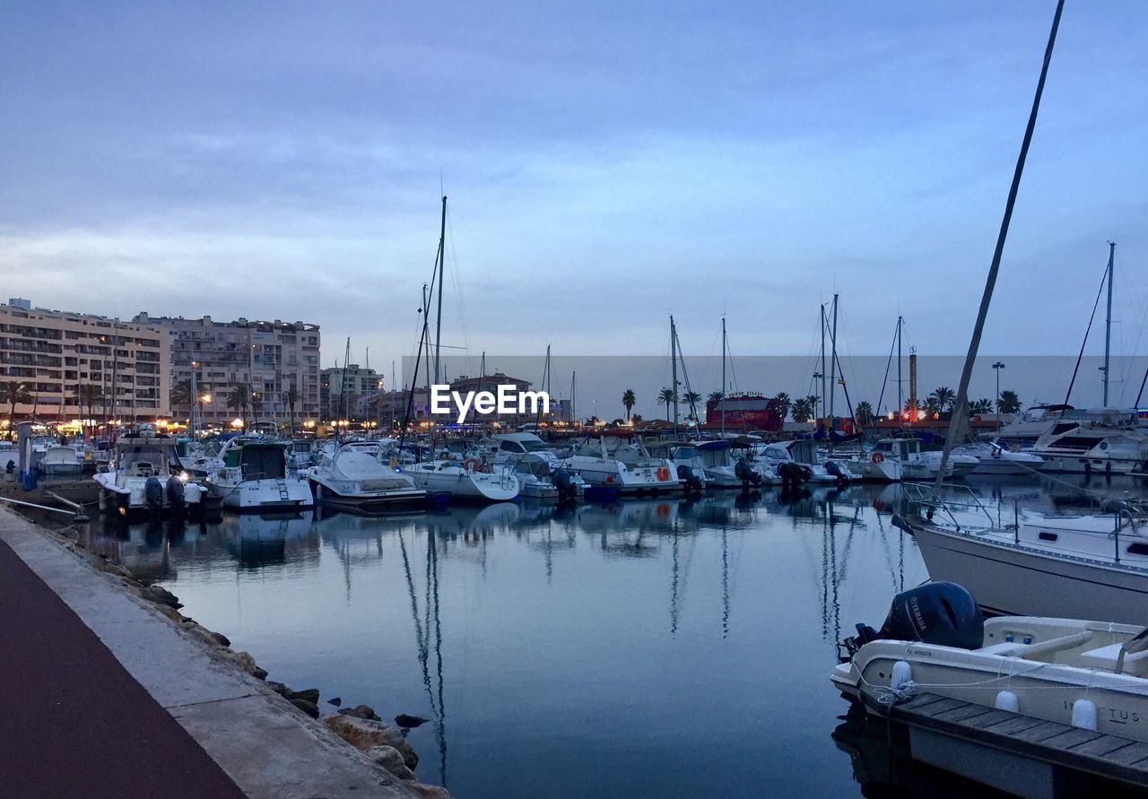 SAILBOATS MOORED IN HARBOR AGAINST SKY