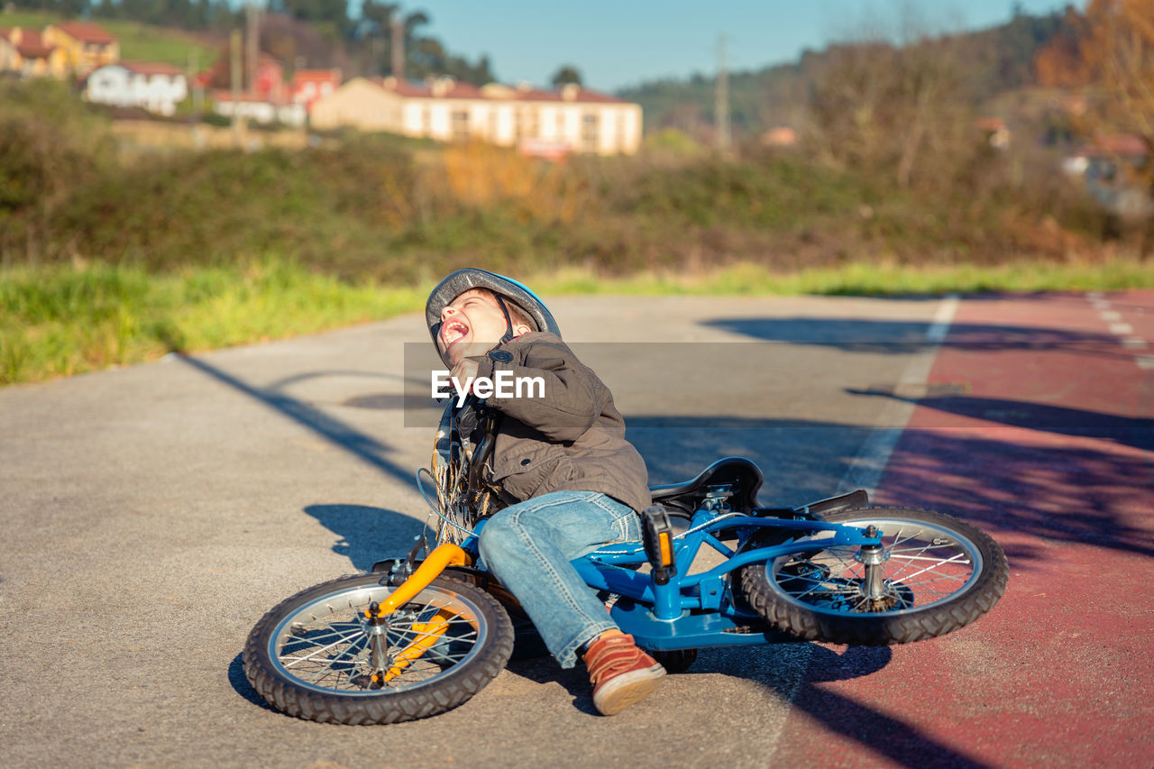 Fallen boy with bicycle screaming on road in city