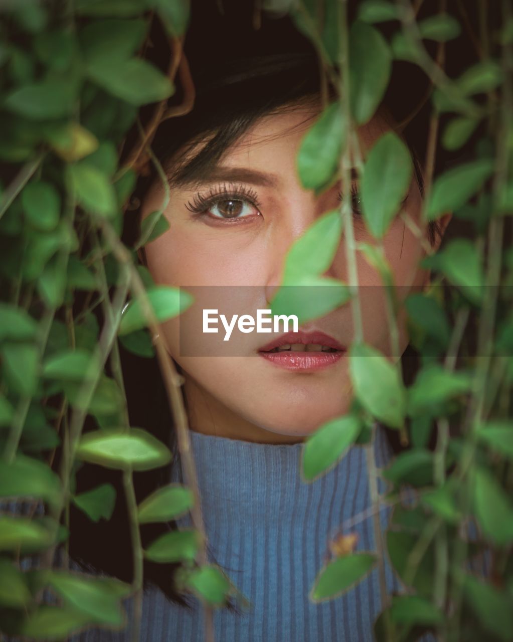 Close-up portrait of young woman seen through leaves