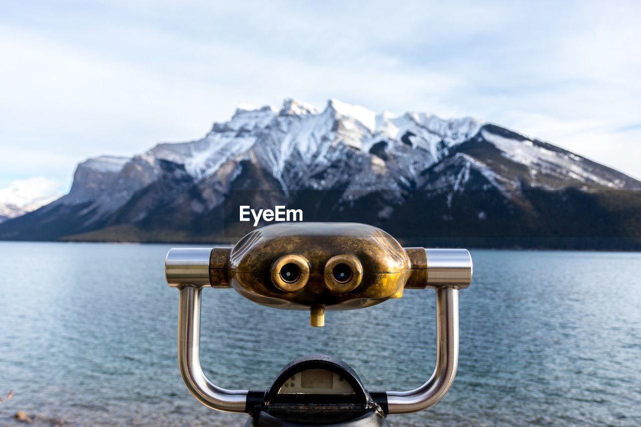 Close-up of coin-operated binoculars by lake against mountain