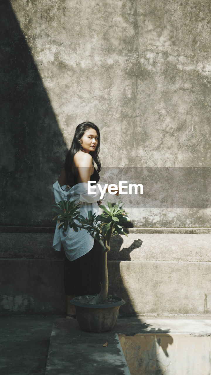 Woman standing by potted plant against wall