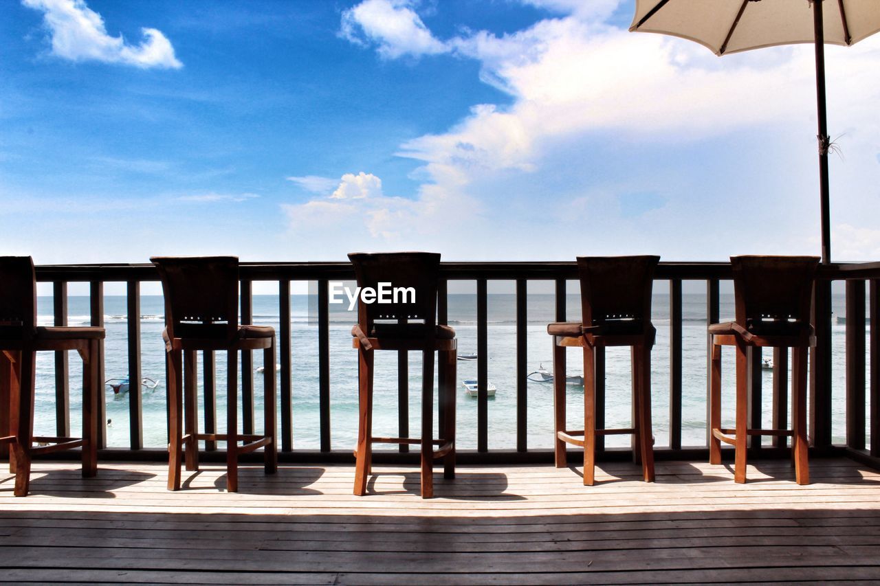 WOODEN CHAIRS ON BEACH AGAINST SKY