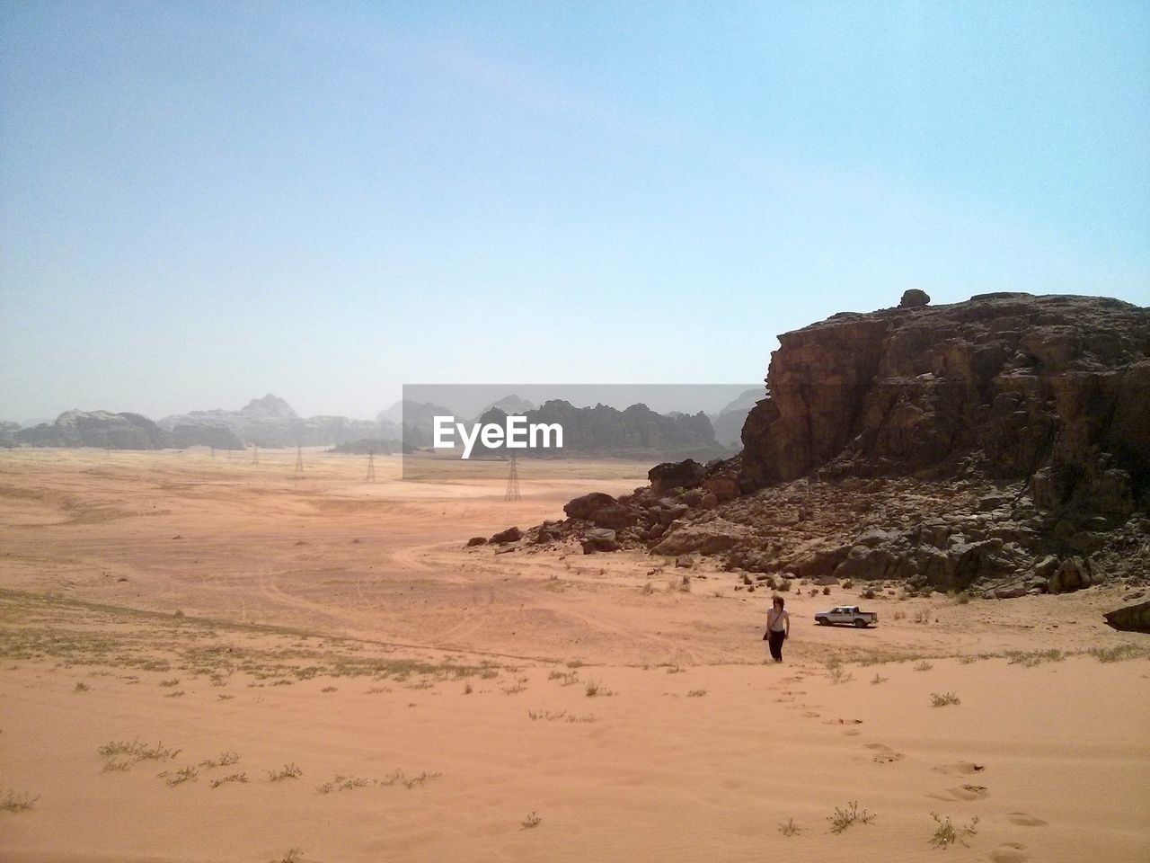 Woman walking on barren landscape against clear sky