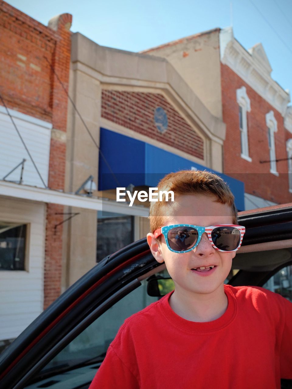 Portrait of boy wearing sunglasses while standing by car in city