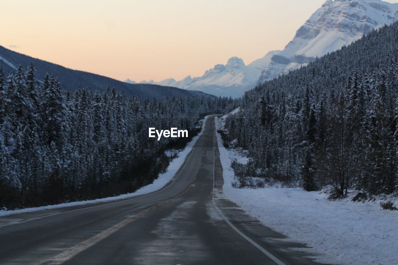 EMPTY ROAD ALONG SNOW COVERED MOUNTAIN