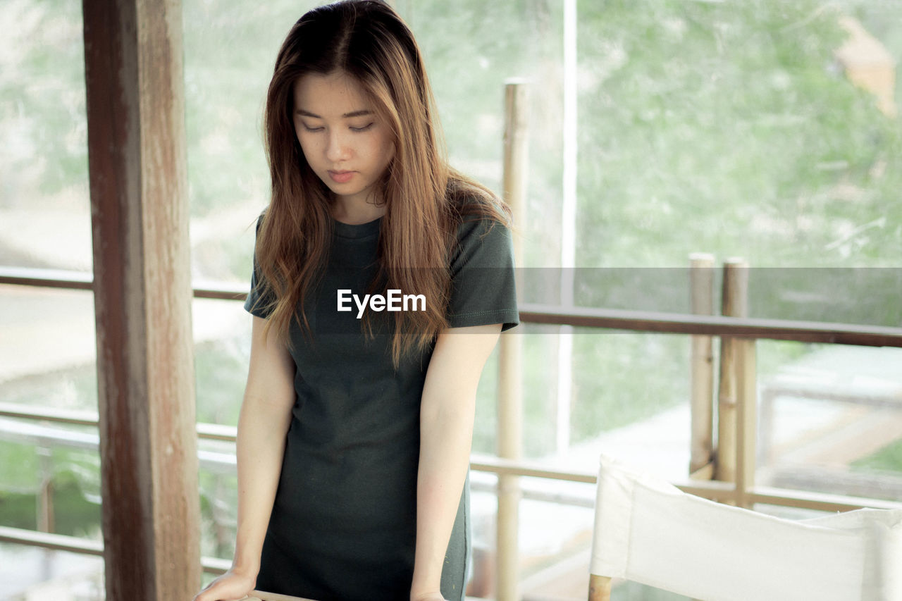 Young woman looking down while standing at table against balcony