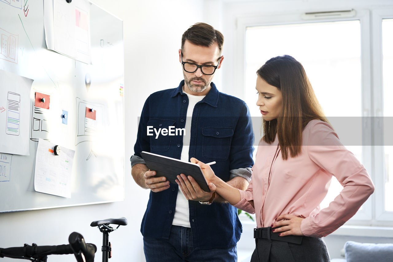 Two colleagues at whiteboard sharing tablet in office