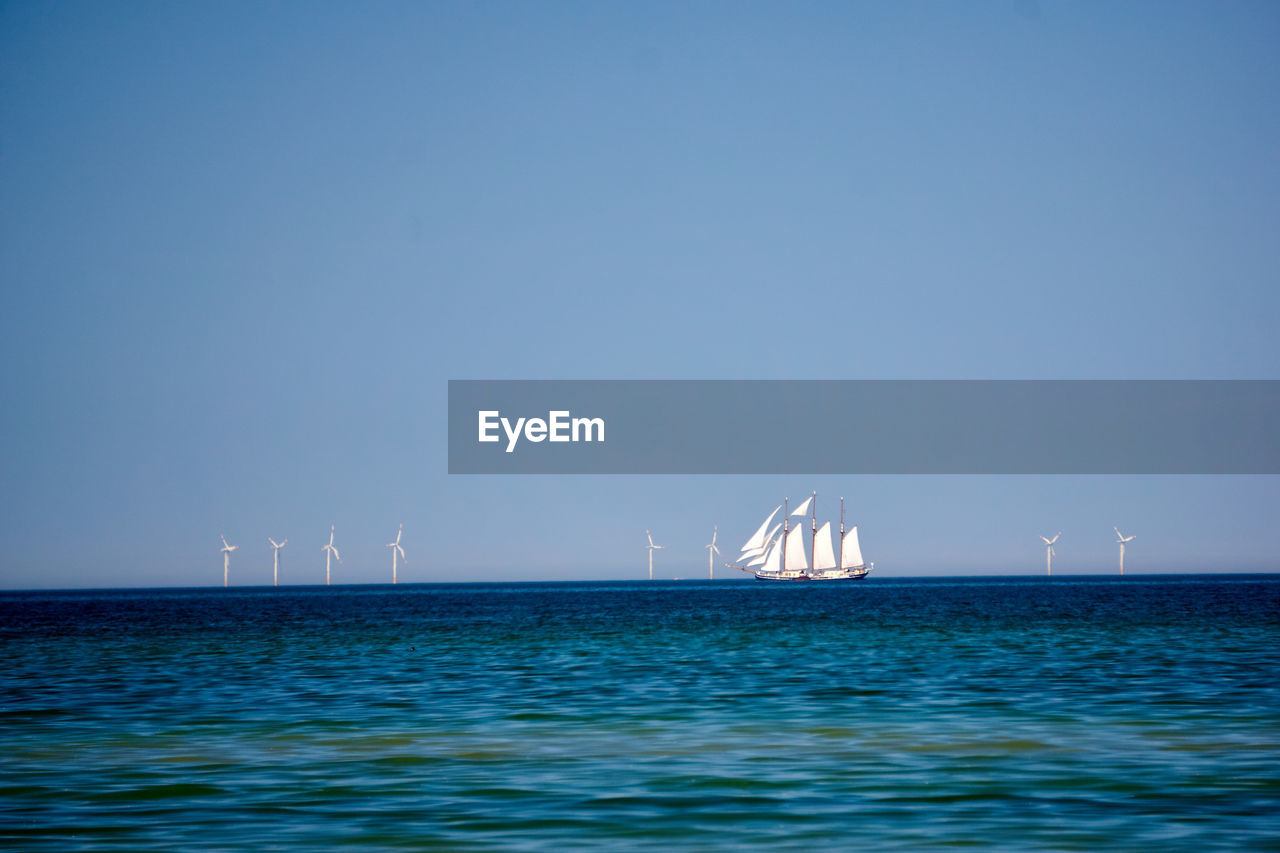 Sailboat in sea against clear blue sky