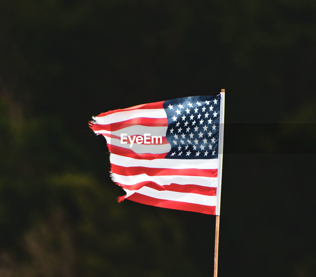 Torn american flag against sky at dusk