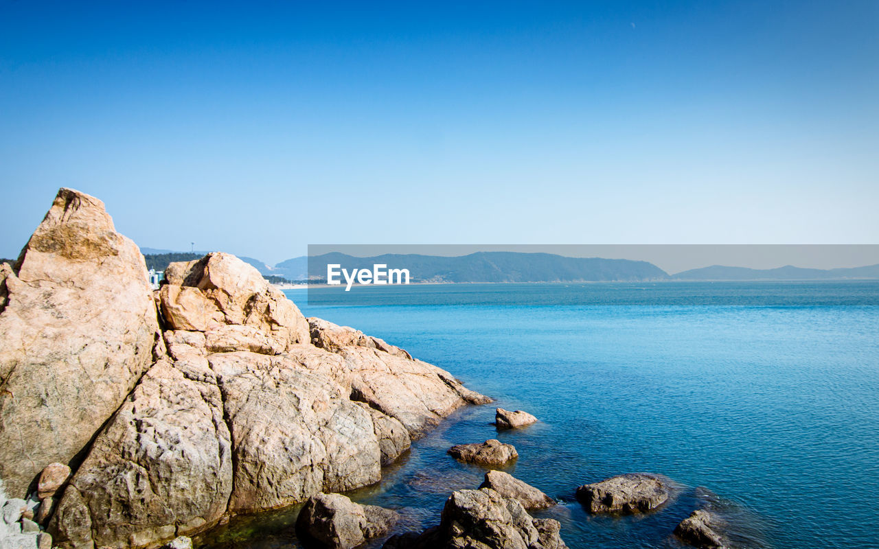 PANORAMIC VIEW OF ROCKS AND SEA AGAINST BLUE SKY