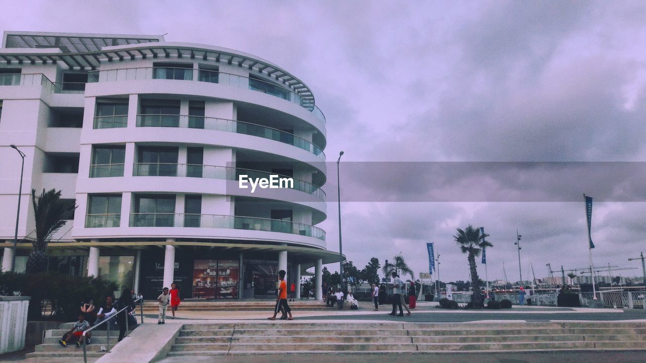 PEOPLE ON STREET BY MODERN BUILDINGS AGAINST SKY