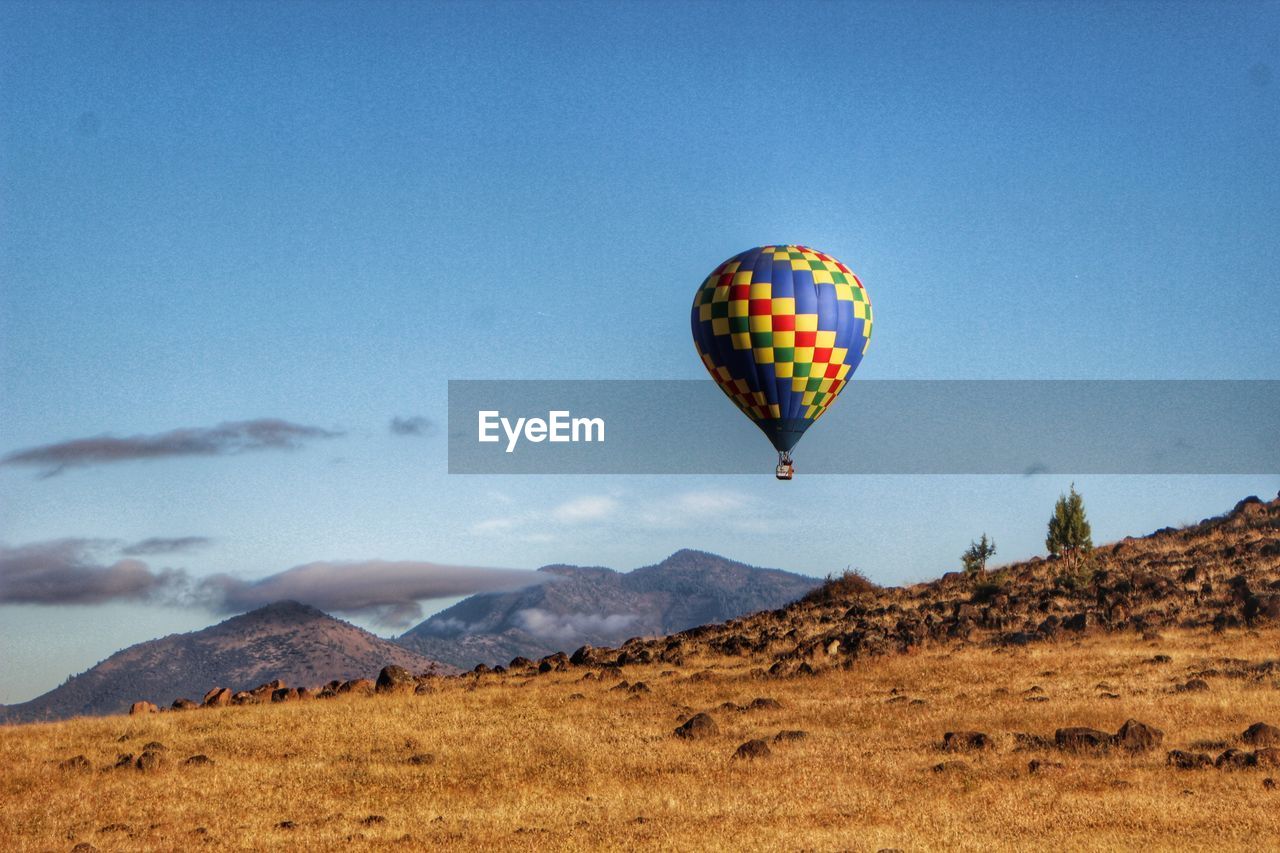 Colorful hot air balloon flying over field against sky
