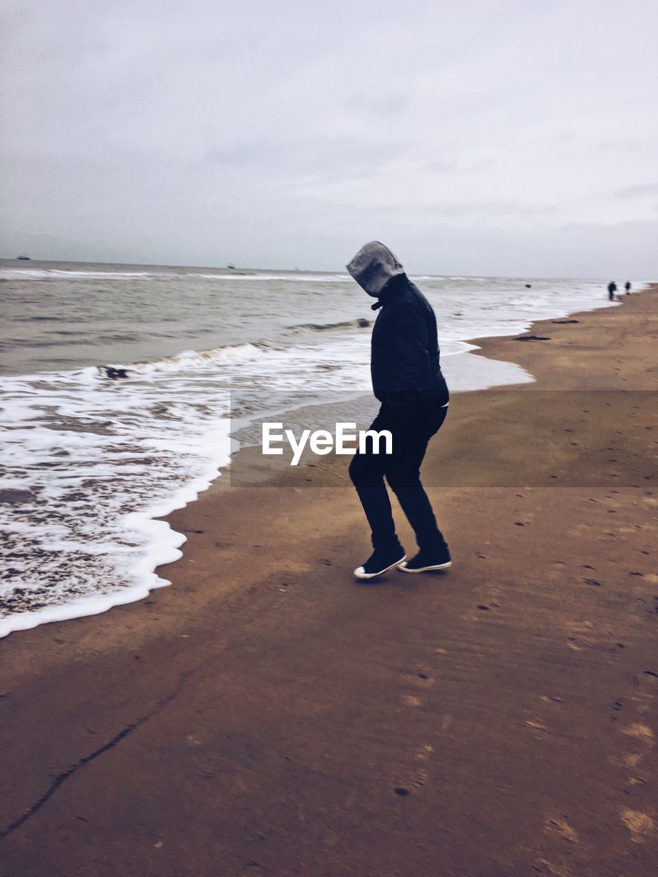 BOY STANDING ON BEACH AGAINST SKY