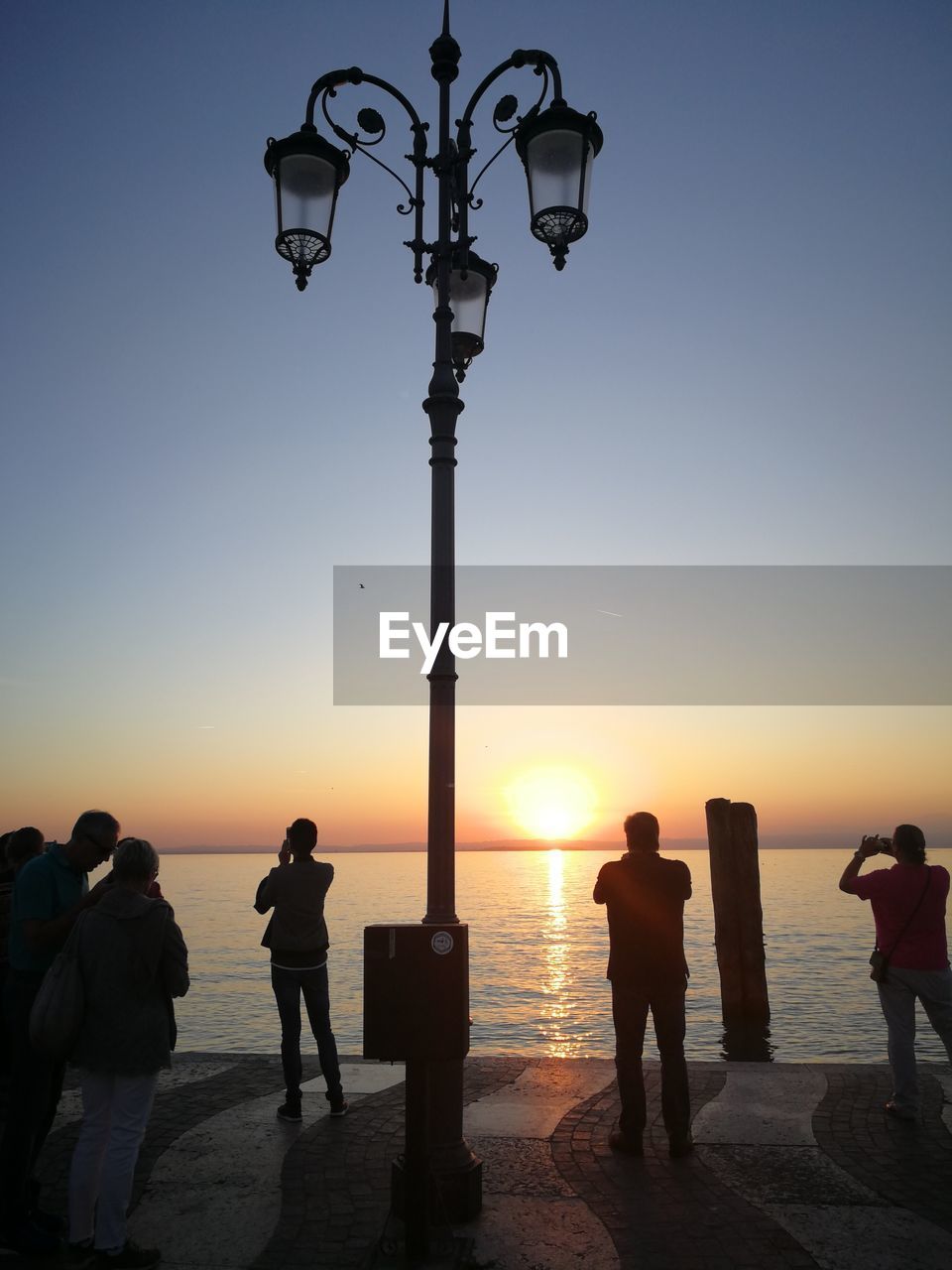 SILHOUETTE PEOPLE ON STREET AGAINST SEA AT SUNSET