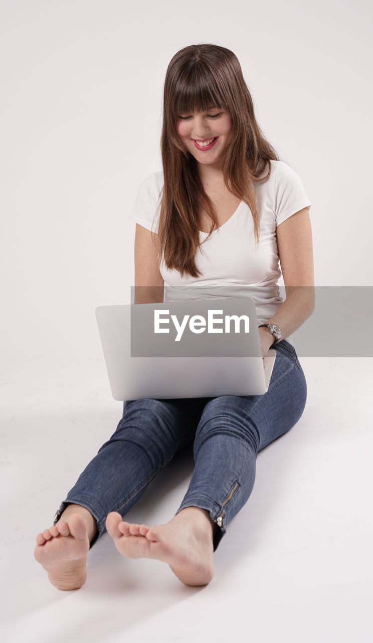 Happy young woman using laptop while sitting against white background