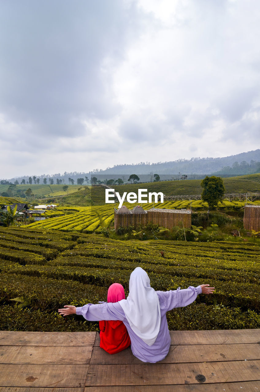 sky, cloud, nature, landscape, environment, adult, religion, one person, hill, plant, rural area, rear view, flower, land, rural scene, full length, tranquility, beauty in nature, scenics - nature, spirituality, agriculture, women, sitting, lifestyles, morning, relaxation, leisure activity, field, tranquil scene, day, outdoors, belief, food and drink, clothing, grass, travel, vacation, trip, holiday, travel destinations, tree, sunlight, green, crop