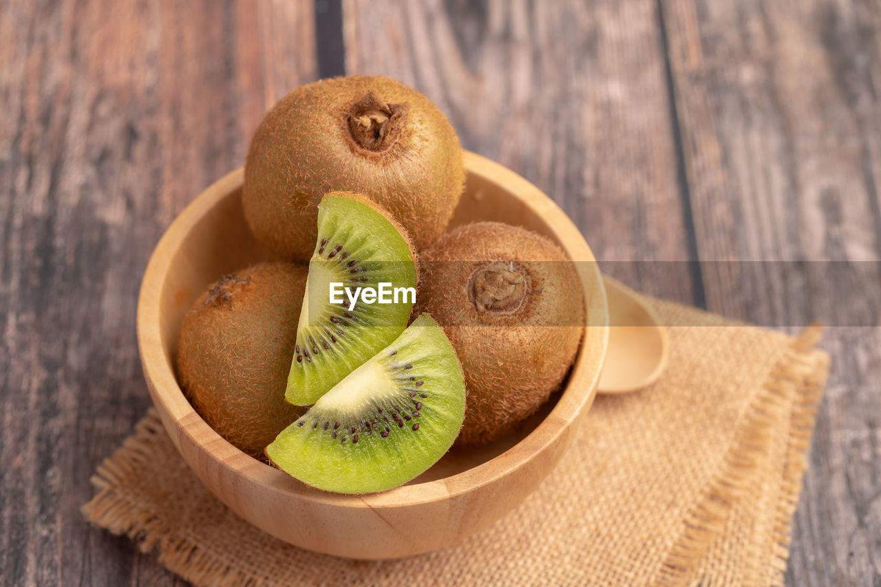 Slices of fresh kiwi in a wood bowl placed on the old wooden table