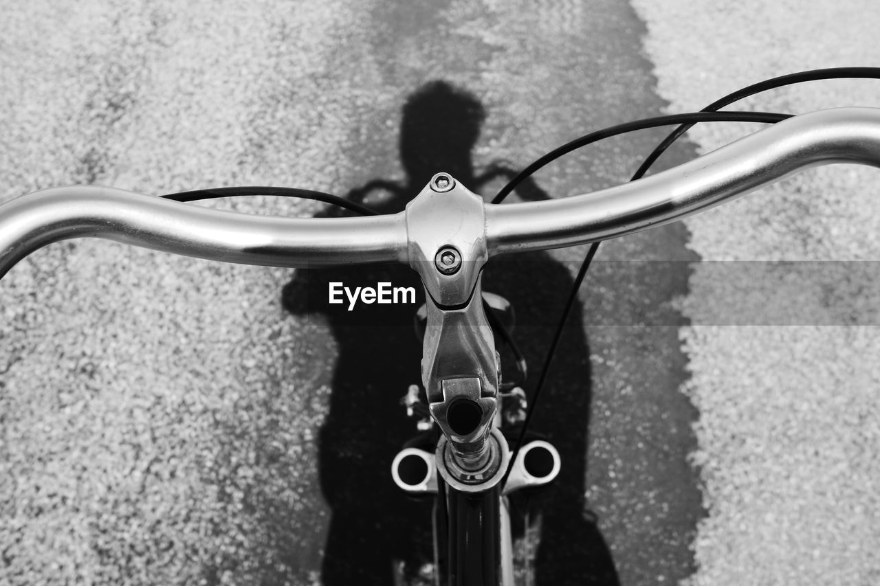 Close-up of bicycle handlebar with shadow of person riding bicycle seen on road
