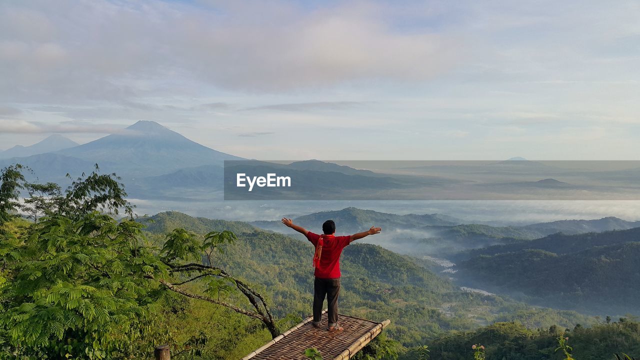 Rear view of man with arms outstretched standing against mountains