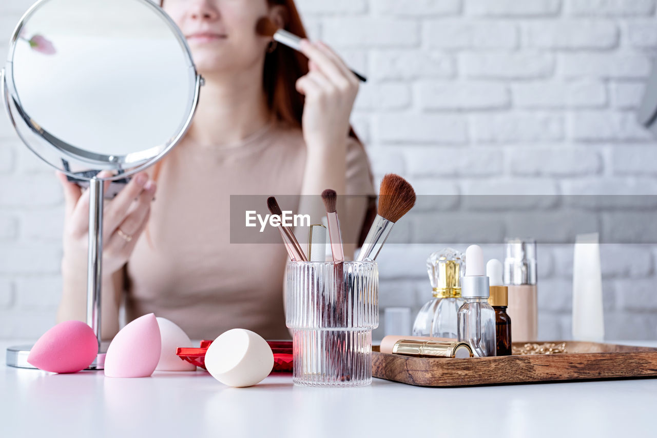 Young beautiful woman holding make-up brushes and making up with cosmetics set at home