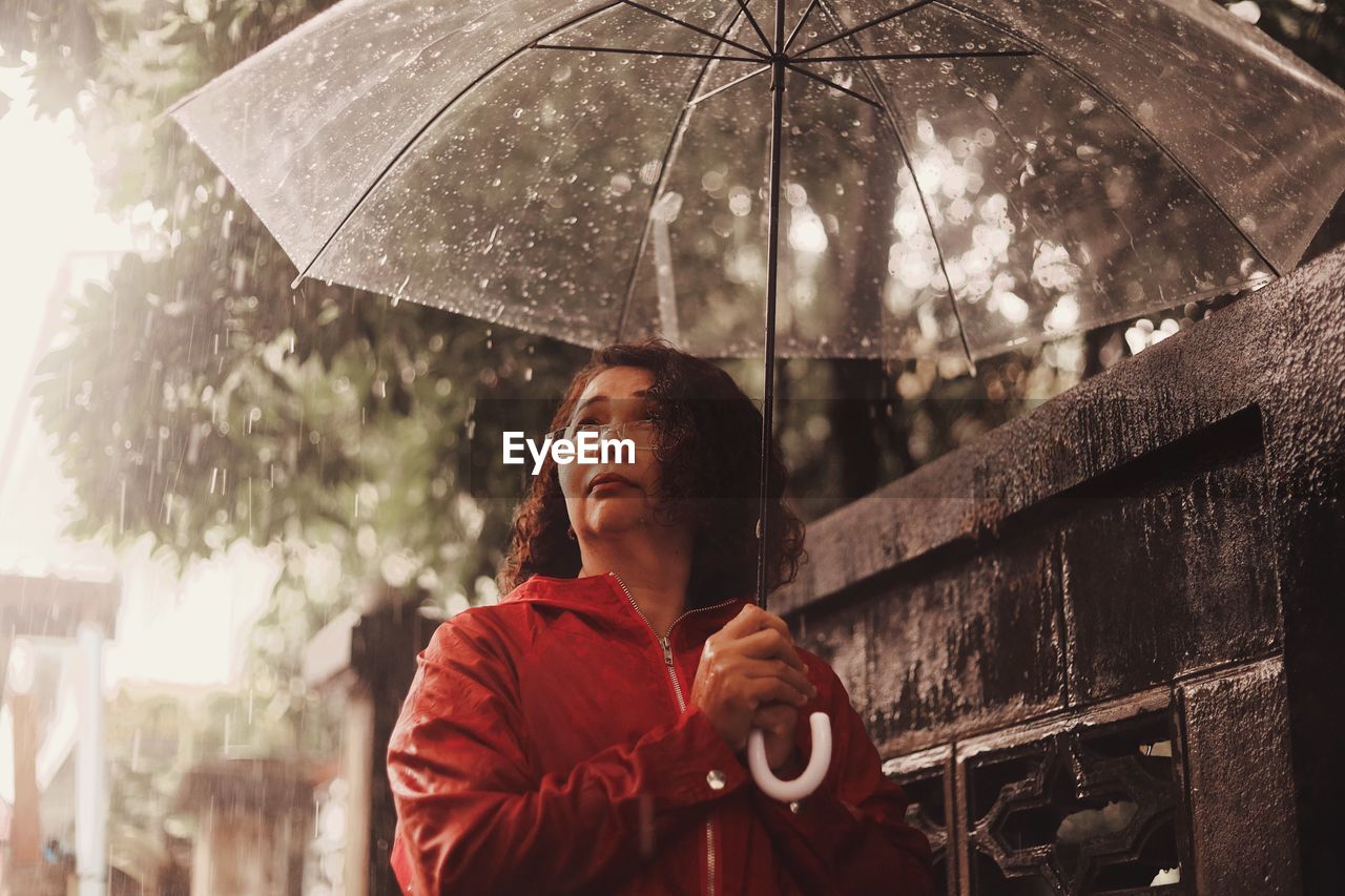 Woman carrying umbrella while standing by retaining wall during monsoon