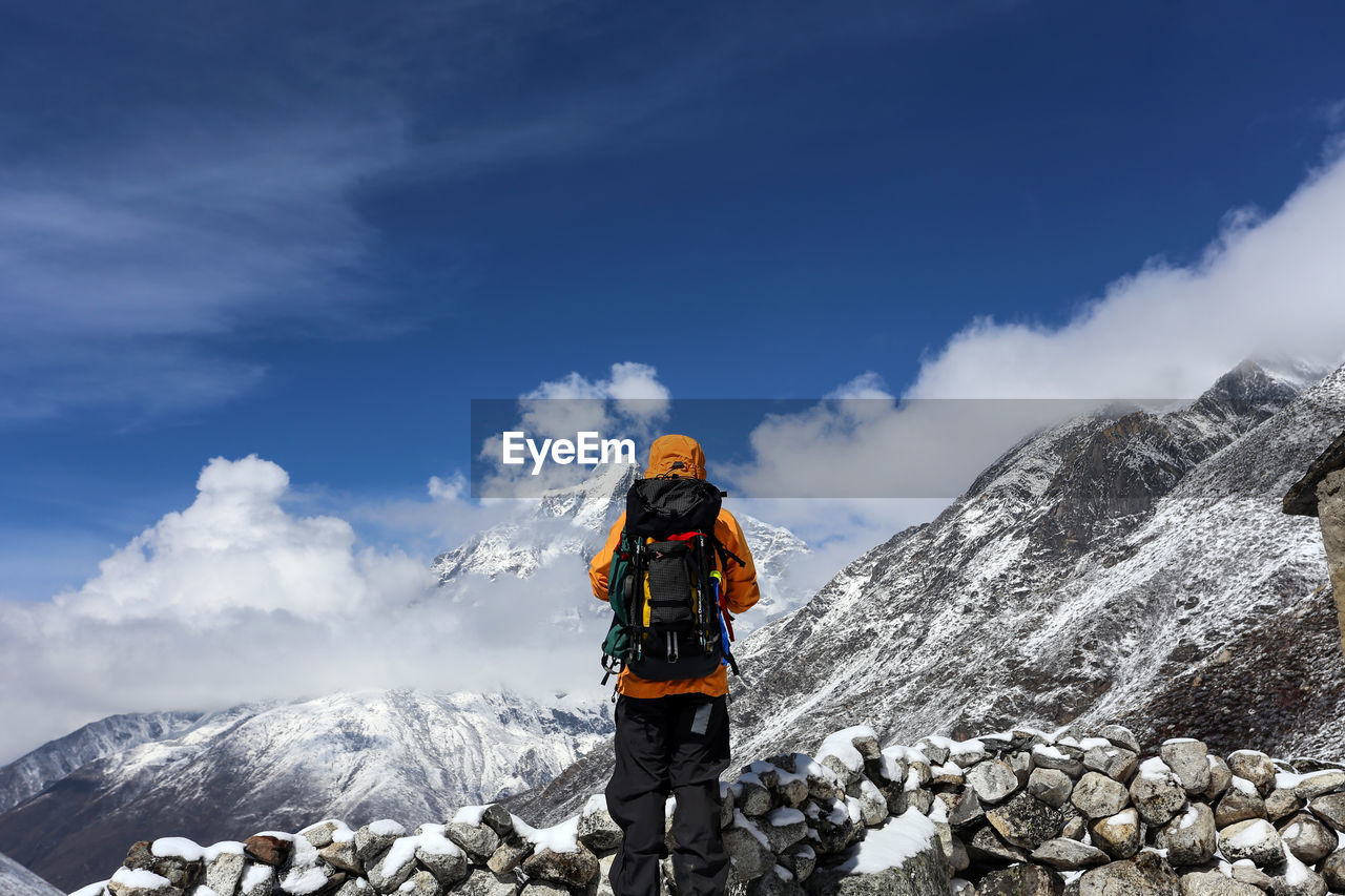 Rear view of hiker carrying backpack while standing on snow covered mountain