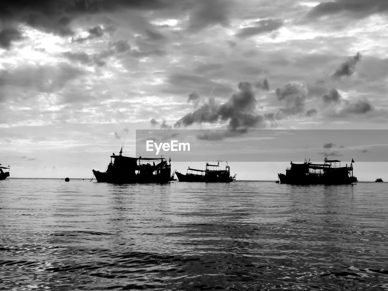 Boats in calm sea against cloudy sky