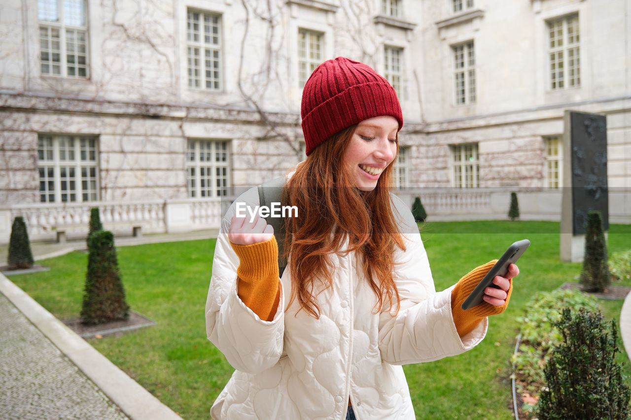 young woman using mobile phone in front of building