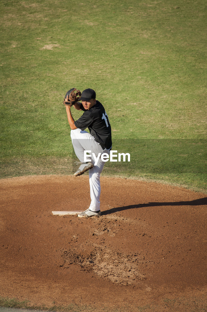 Teen baseball player in black and white uniform in full wind up on the mound