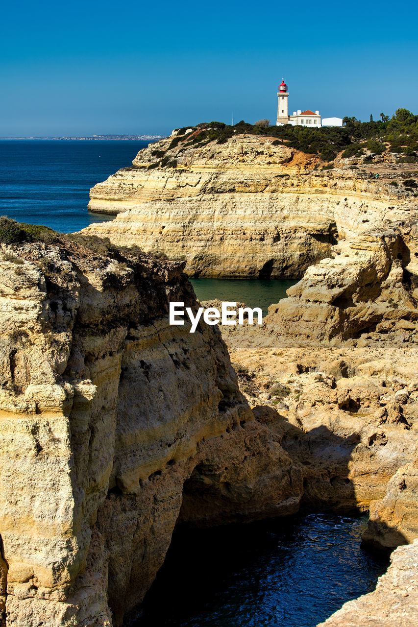 Lighthouse on rocks by sea against sky