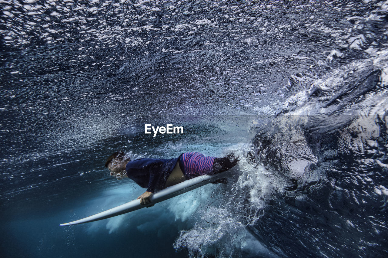 Male surfer with surfboard on wave undersea