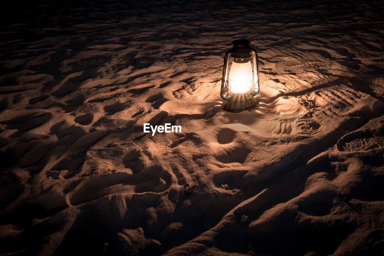 HIGH ANGLE VIEW OF ILLUMINATED LIGHT BULBS ON BEACH