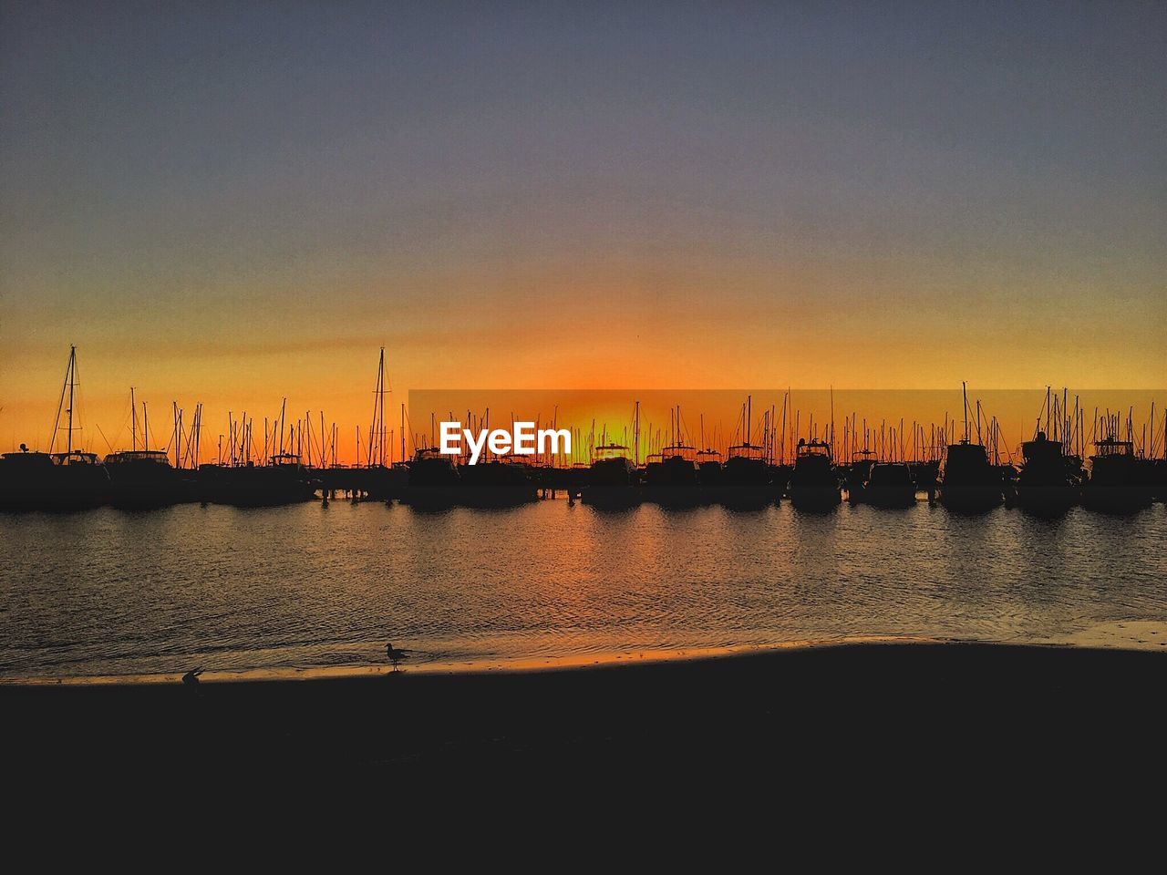 Sailboats moored on sea against sky during sunset