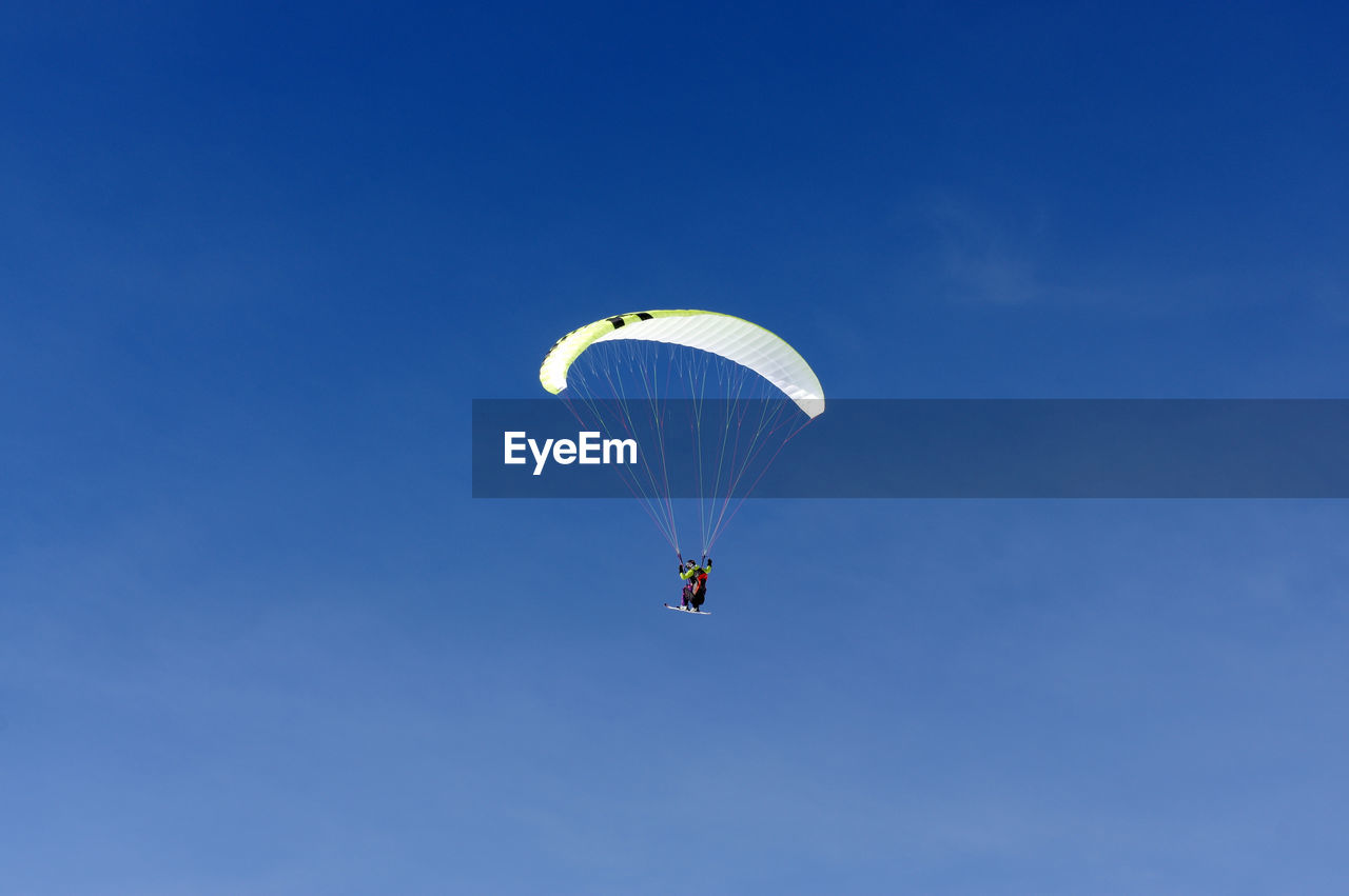 Low angle view of person paragliding against blue sky