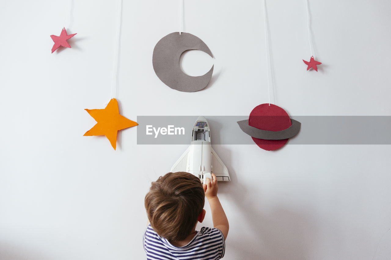 Rear view of boy holding toy rocket over wall with galaxy decoration