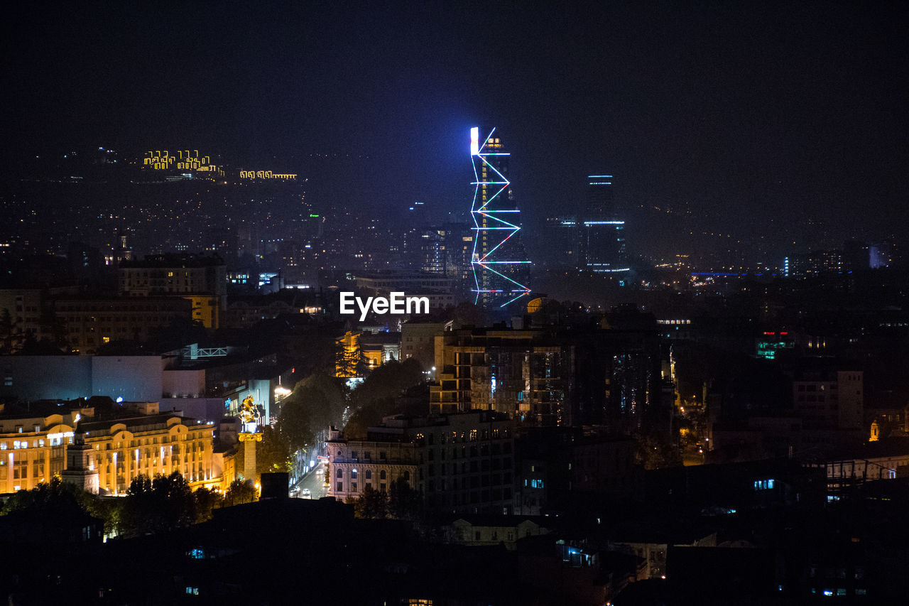 HIGH ANGLE VIEW OF ILLUMINATED CITY BUILDINGS AT NIGHT