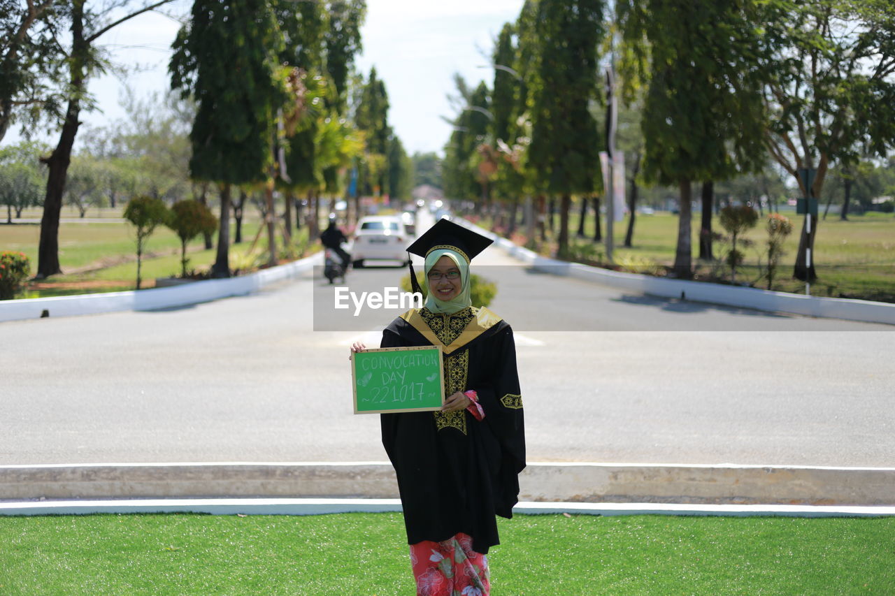 Portrait of woman in graduation gown standing on field