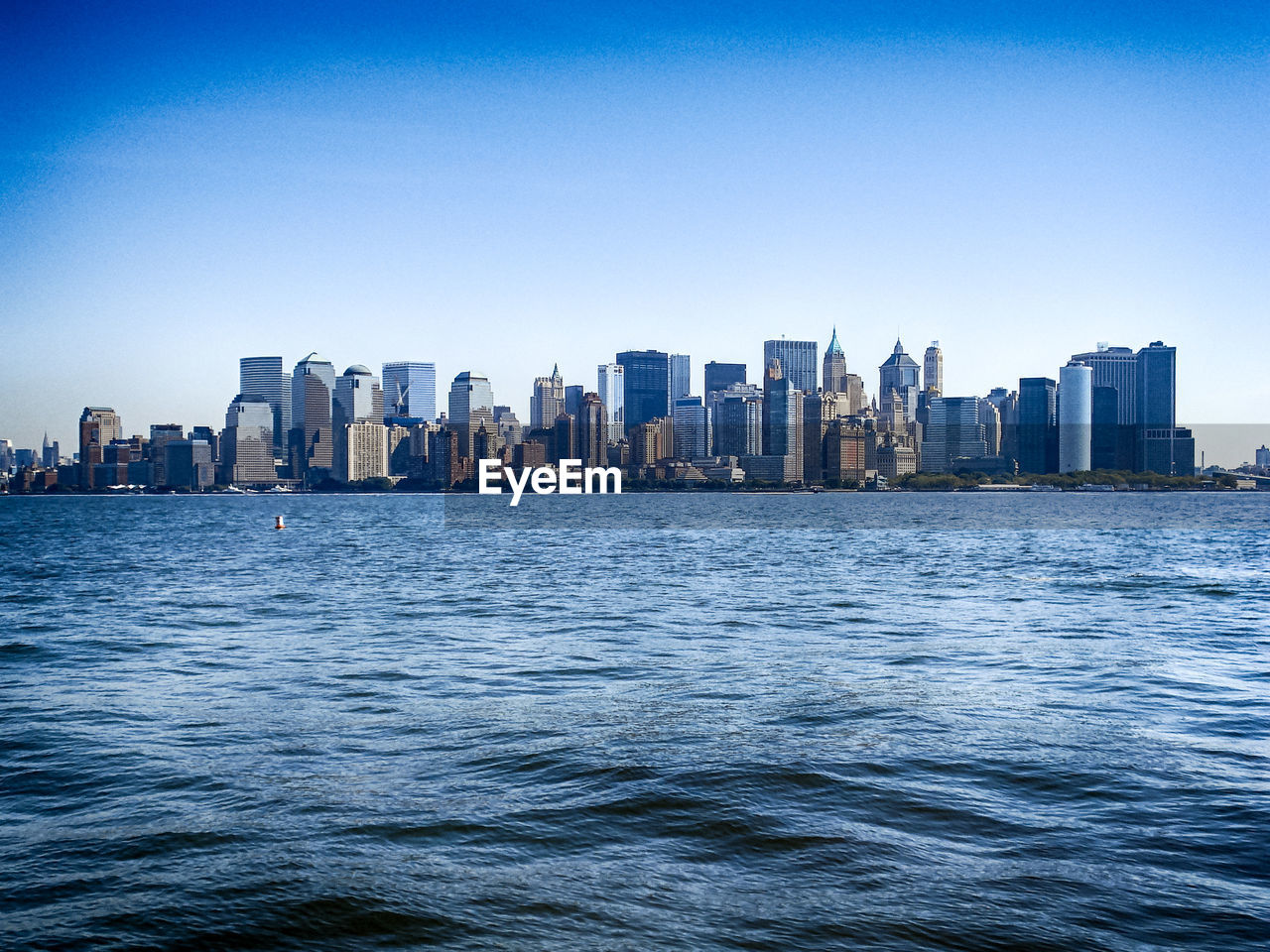 City skyline by river against clear blue sky