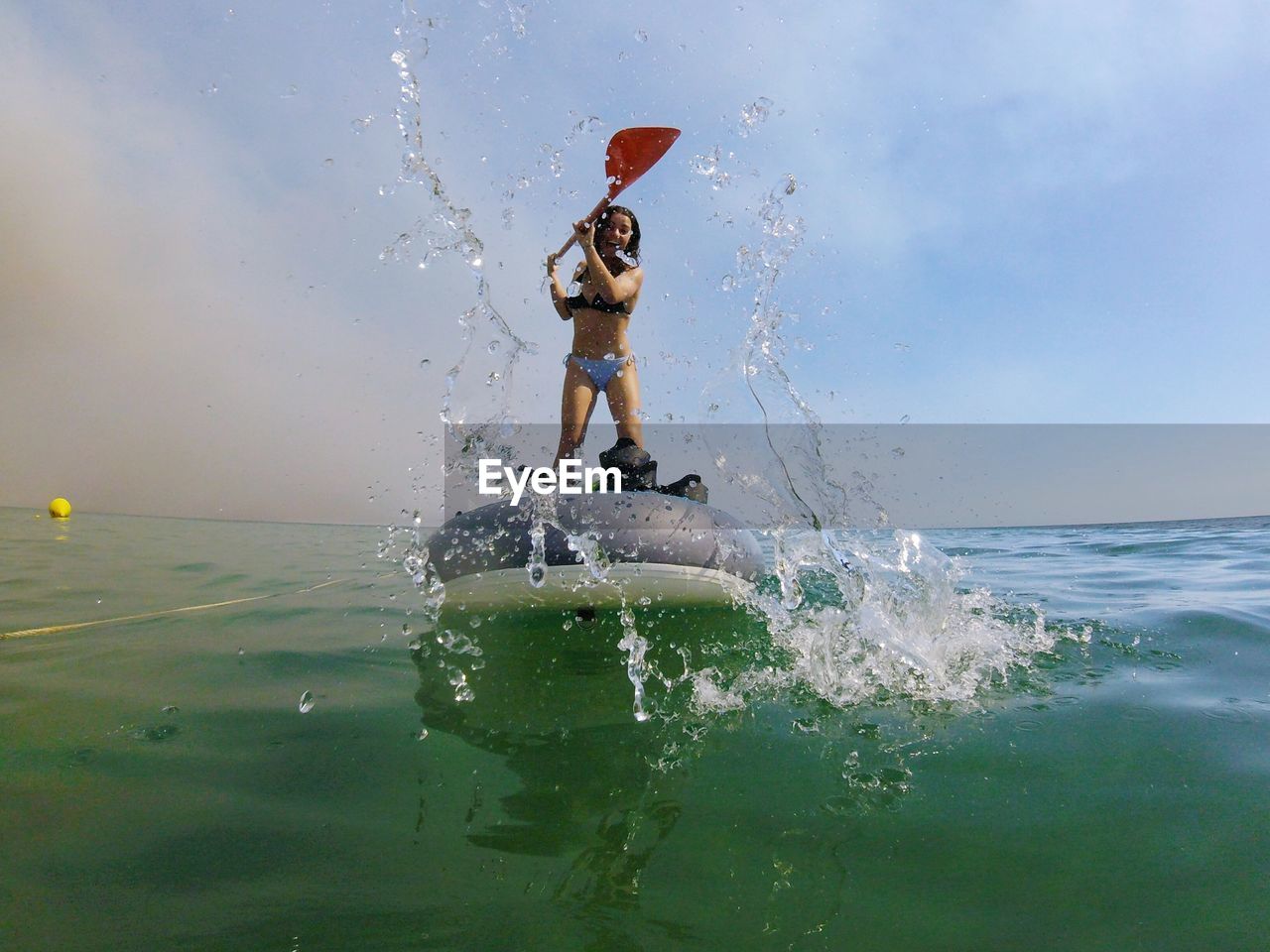 Cheerful young woman standing on inflatable raft in sea against sky