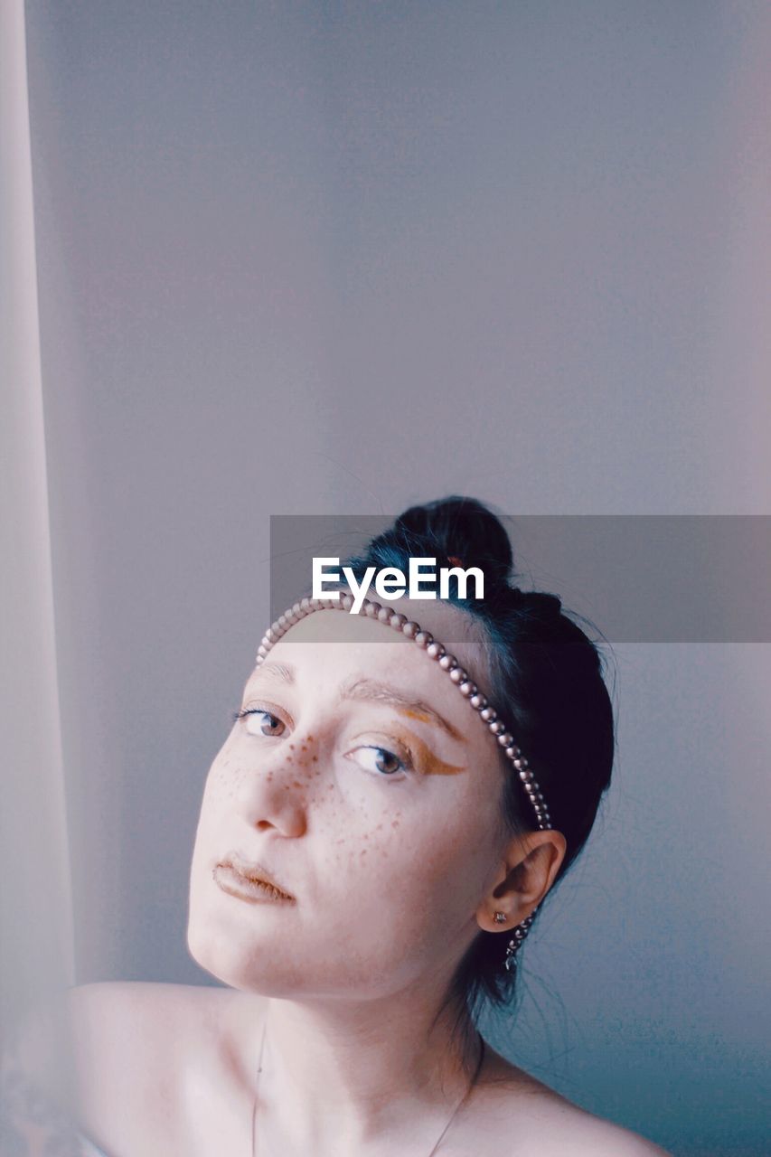 PORTRAIT OF YOUNG WOMAN AGAINST WALL
