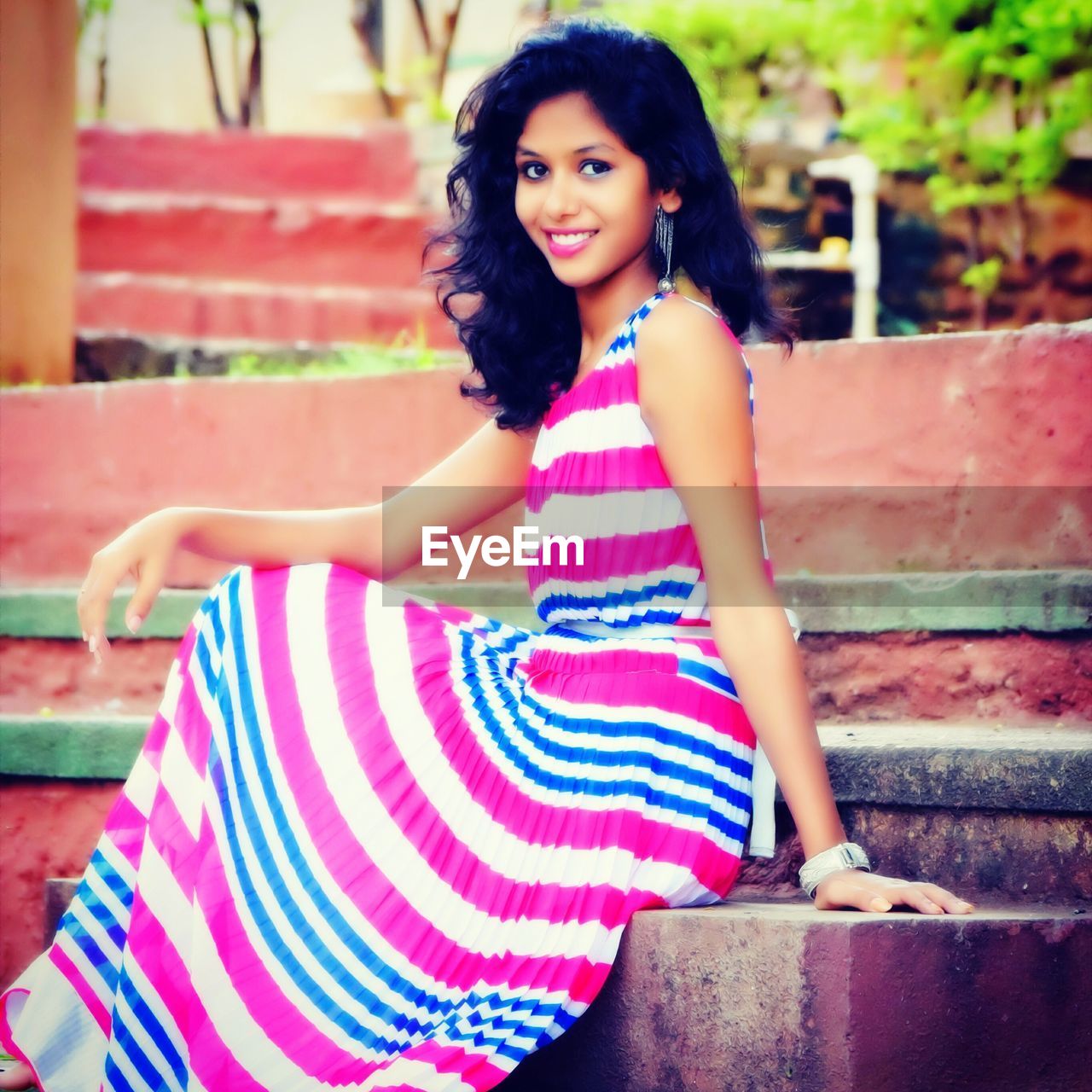 PORTRAIT OF SMILING YOUNG WOMAN SITTING ON MULTI COLORED